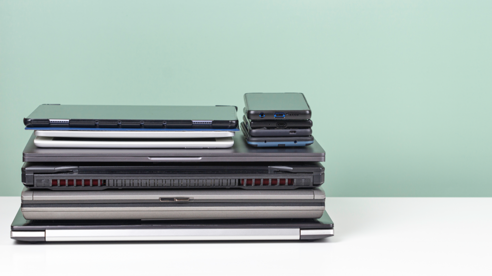 Pile of old used laptop computers, digital tablets, smartphones for recycling on white table. Planned obsolescence, e-waste, electronic waste for reuse and recycle concept