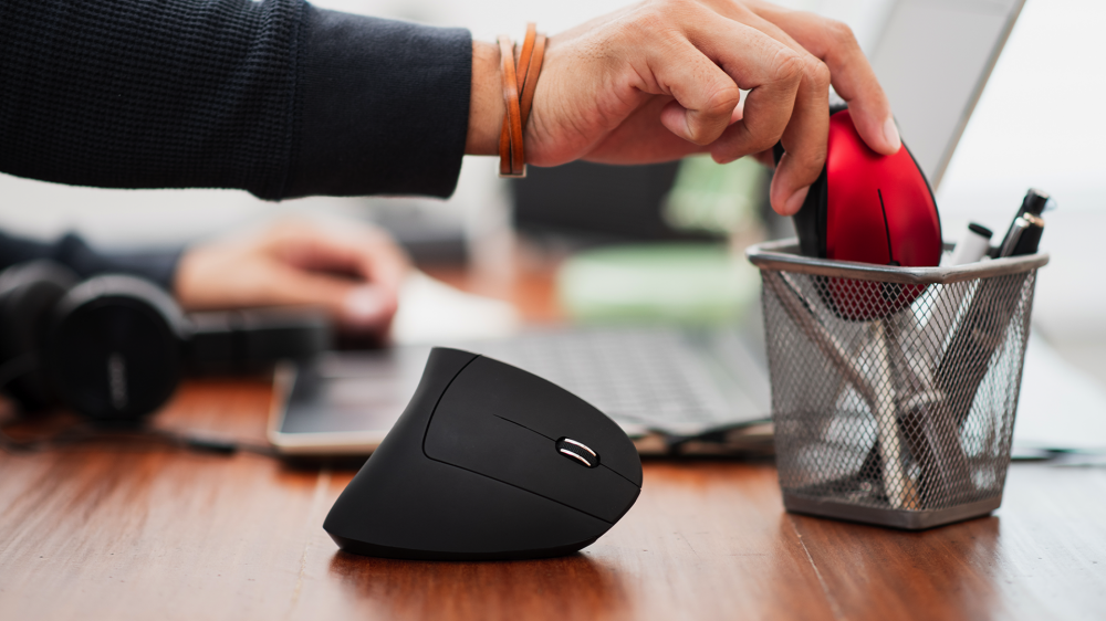 An office working putting away their old mouse after getting a vertical mouse.