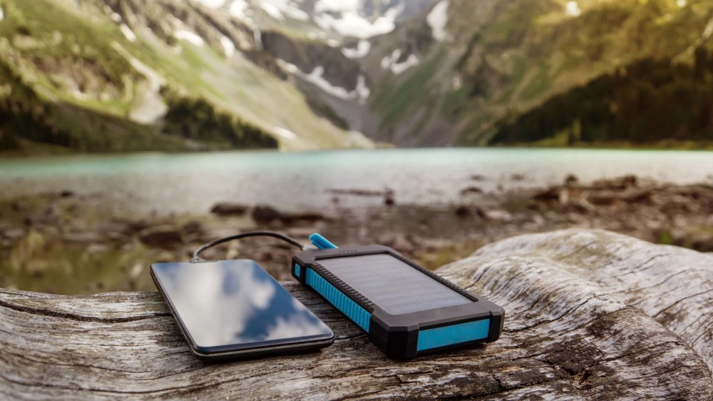 a smartphone charging with a portable charger on a log outside in the mountains.